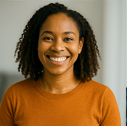 “Smiling woman in an orange sweater looking toward the camera against a softly lit background.”