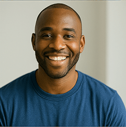“Smiling man in a blue shirt looking toward the camera against a softly lit neutral background.”