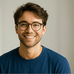 “Smiling young man wearing glasses and a blue sweater, looking toward the camera.”